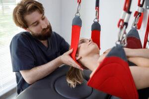 Ein Physiotherapeut hilft einer Patientin bei der rehabilitativen Physiotherapie an einem Schwebeseilsystem. Moderne Klinik mit fortschrittlicher rehabilitativer Therapie.