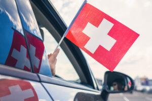 Frau oder Mädchen hält Schweizer Flagge aus dem offenen Autofenster.