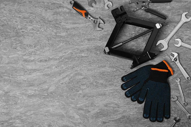 Auto-Scherenwagenheber, Handschuhe und verschiedene Werkzeuge auf grauer Stein-Oberfläche