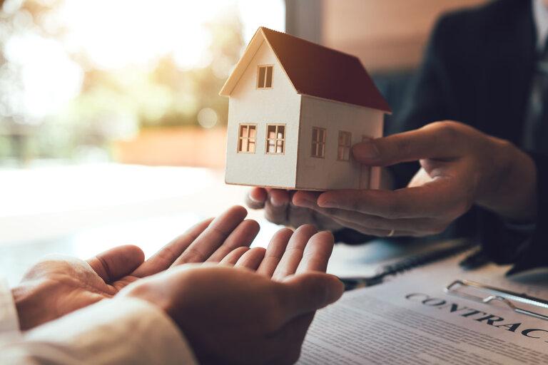 Der Immobilienmakler beglückwünscht den neuen Käufer, indem er dem Kunden im Büro des Maklers ein Hausmodell überreicht.