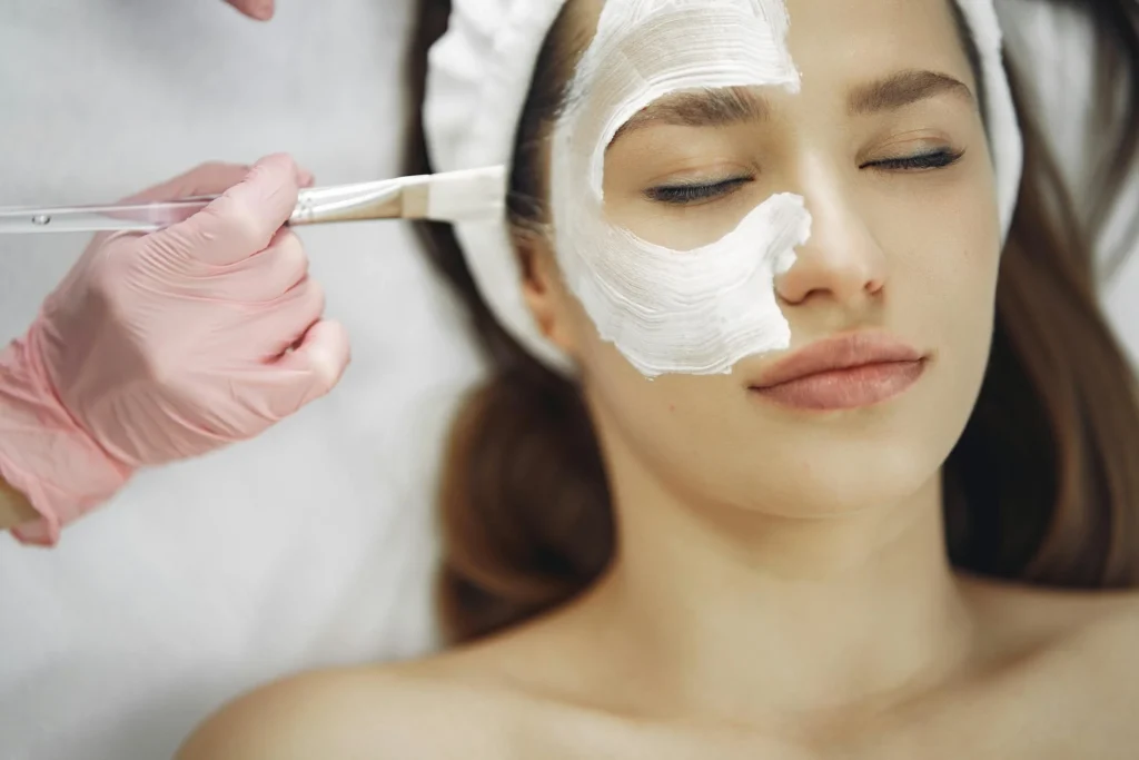 Anwendung eines Gesichtspeelings mit Niacinamide Serum auf die Haut einer entspannten Frau während einer professionellen Gesichtsbehandlung