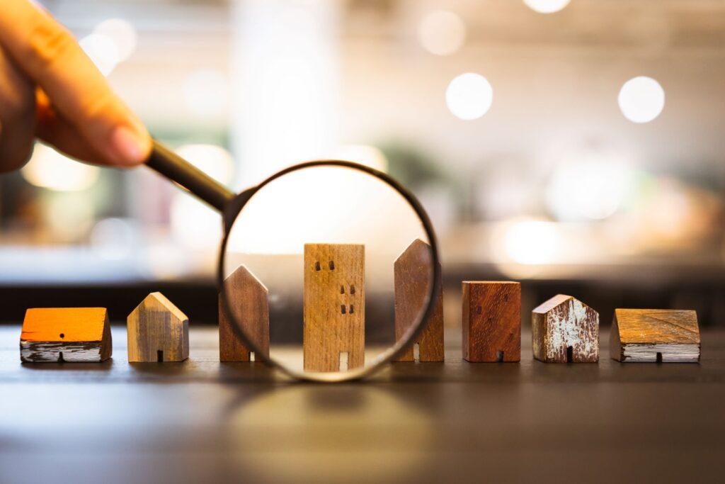 Hand hält Vergrößerungsglas und Blick auf Haus-Modell, Haus Auswahl, Immobilien-Konzept.