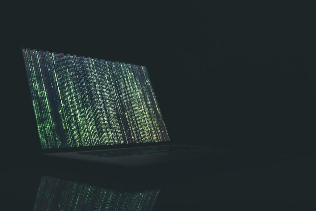 Laptopbildschirm mit grünem Binärcode in dunkler Umgebung, symbolisiert die Notwendigkeit von Datenschutzberatung und effektiven IT-Sicherheitsstrategien zum Schutz vor Cyberangriffen.