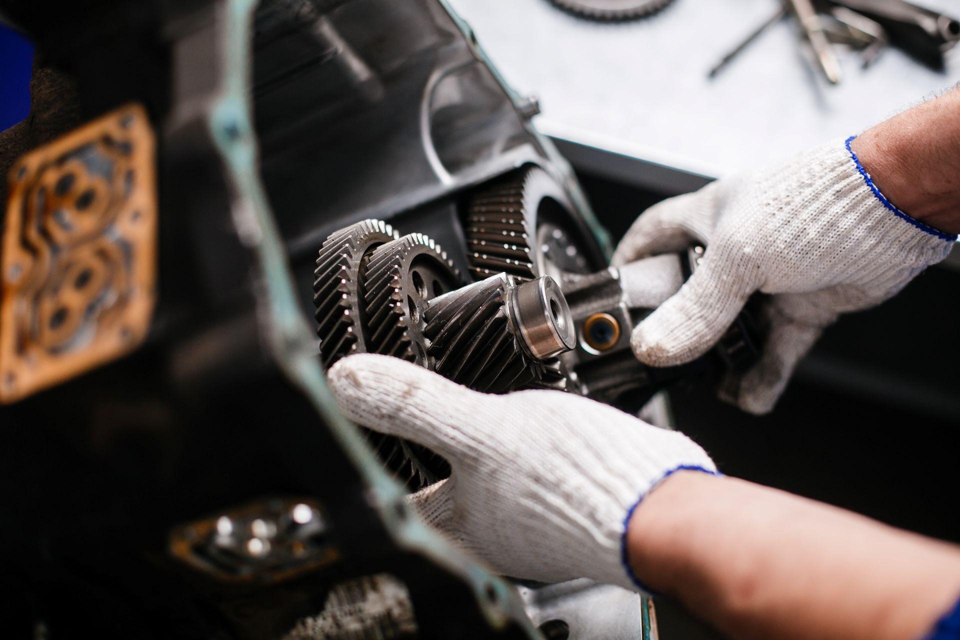 Ein Mechaniker mit Handschuhen montiert Zahnräder in ein Getriebe. Das Bild zeigt präzise Handarbeit und die technischen Details eines komplexen Getriebesystems in der Montagephase.