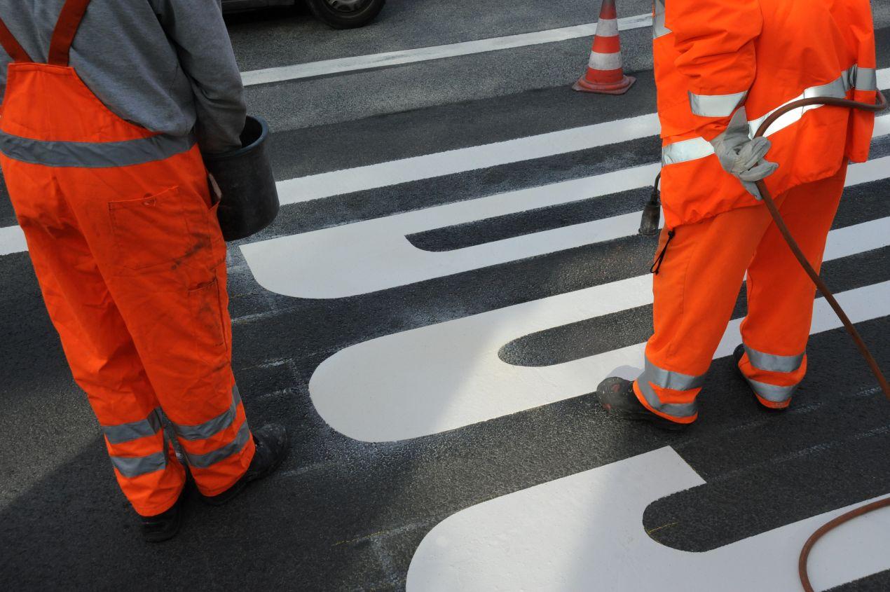 Zwei Arbeiter bringen weisse Bodenmarkierung auf Fahrbahn auf