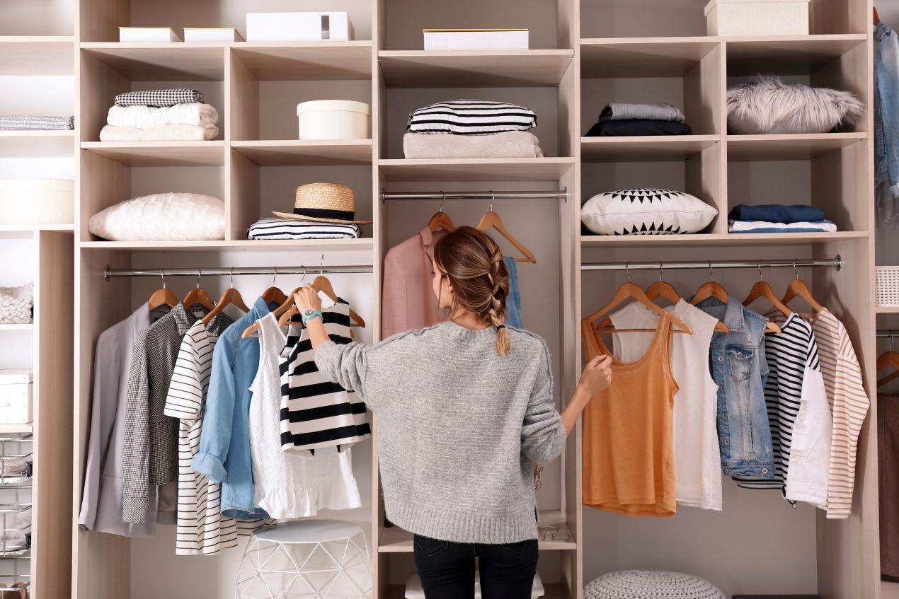 Frau vor offenem Kleiderschrank mit Spiegel beim Sortieren von Kleidung und Accessoires