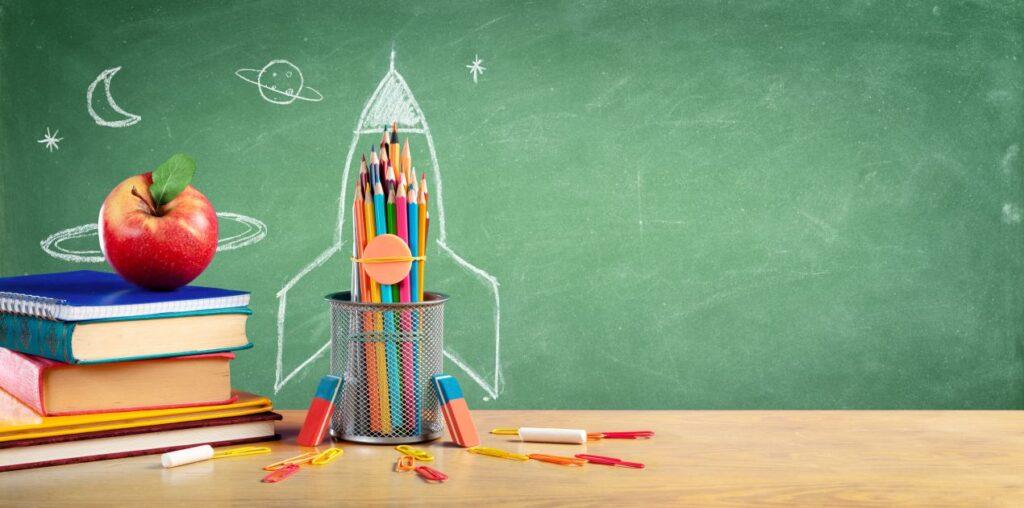 Bunte Stifte, Apfel und Schultafel mit Rakete – Symbolbild fuer Bildung und kosten privatschule berlin