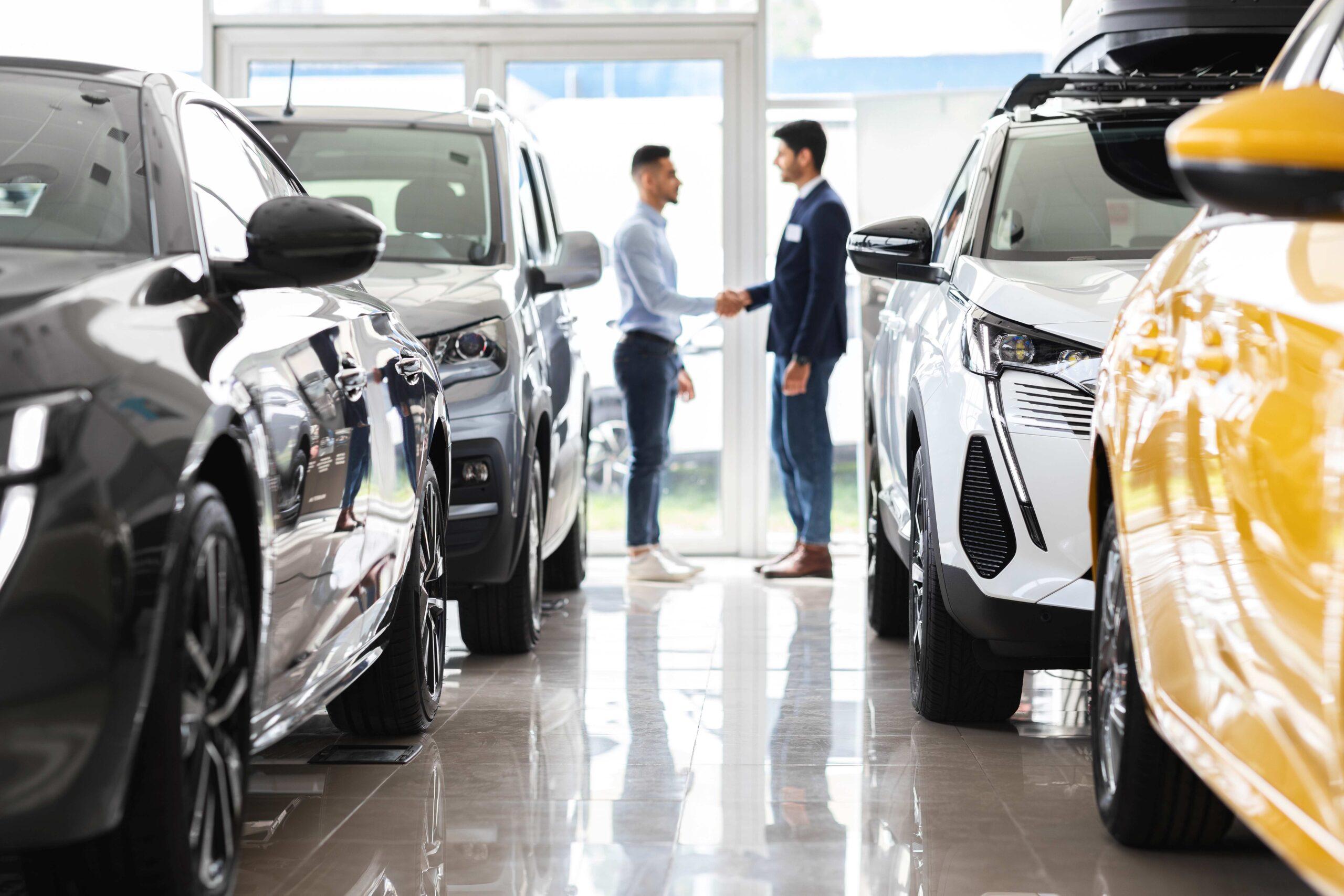 Kunde und Verkaufsassistent schütteln sich die Hände, Innenraum eines Autohauses.